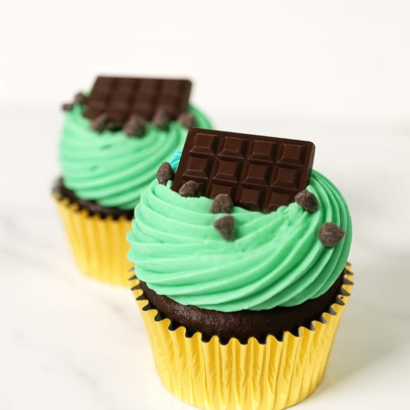 Two Sweet Kneads chocolate cupcakes with green frosting, chocolate chips, and a chocolate bar.