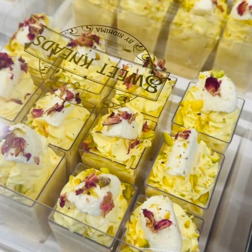 Rows of Sweet Kneads' yellow desserts in clear cups, topped with white cream and rose petals.